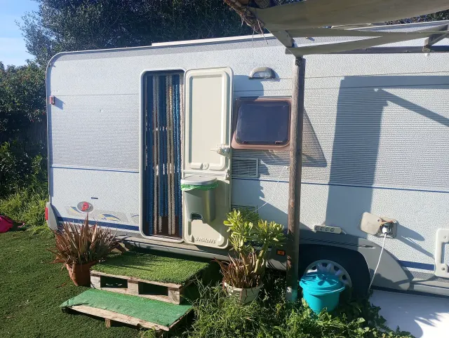 BookNoFees: alojamiento de vacaciones en El Palmar De Vejer – Exterior de una caravana antigua con la puerta abierta, un toldo y plantas en macetas sobre el césped