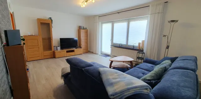 BookNoFees: alojamiento de vacaciones en Langelsheim – Sala con sofá azul, muebles de madera y puerta que da al balcón