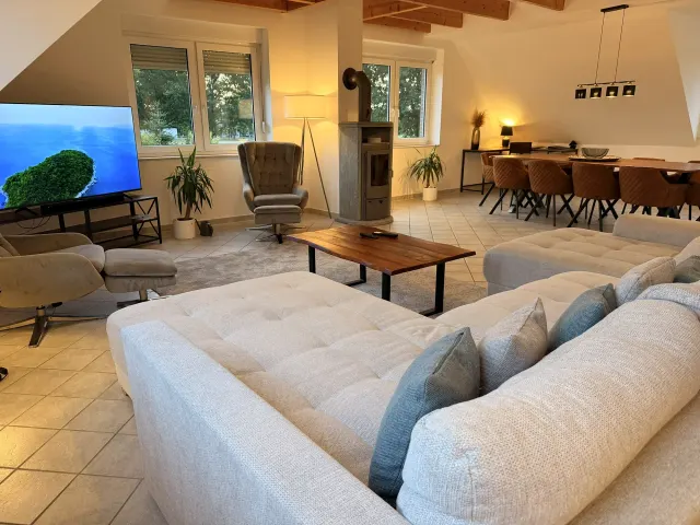 BookNoFees: alojamiento de vacaciones en Stuhr – Sala con sofá en forma de L, estufa de leña y área de comedor con mesa de madera