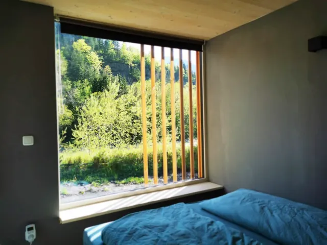 BookNoFees: alojamiento de vacaciones en Hieflau, Estiria, Austria – Habitación con ropa de cama azul y una gran ventana con persianas de madera con vista al bosque